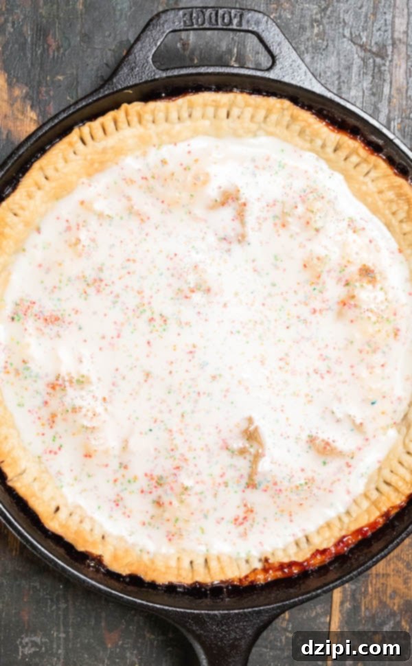 Overhead shot of a beautifully prepared Strawberry Pop-Tart Pie in a cast iron skillet, showcasing its glaze and colorful sprinkles.
