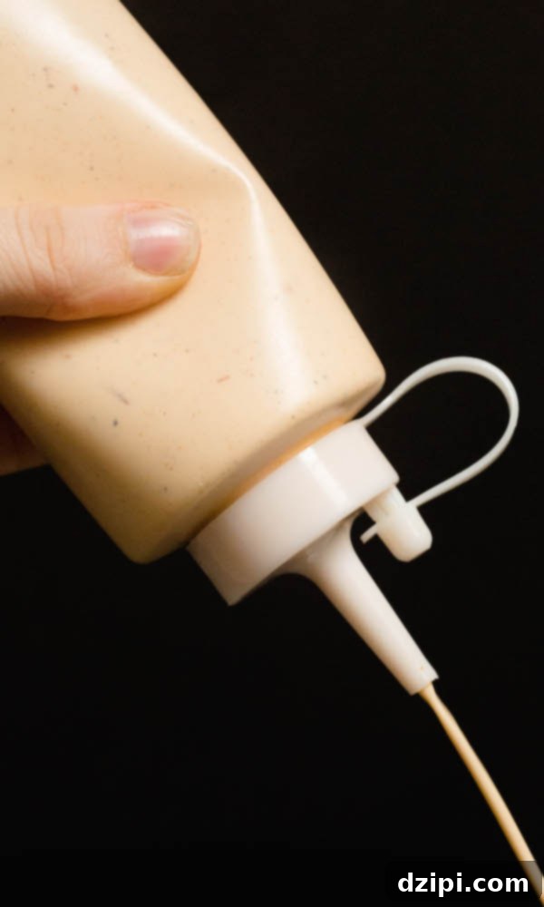 Homemade Alabama White Sauce being squeezed out of a bottle, ready to be served.