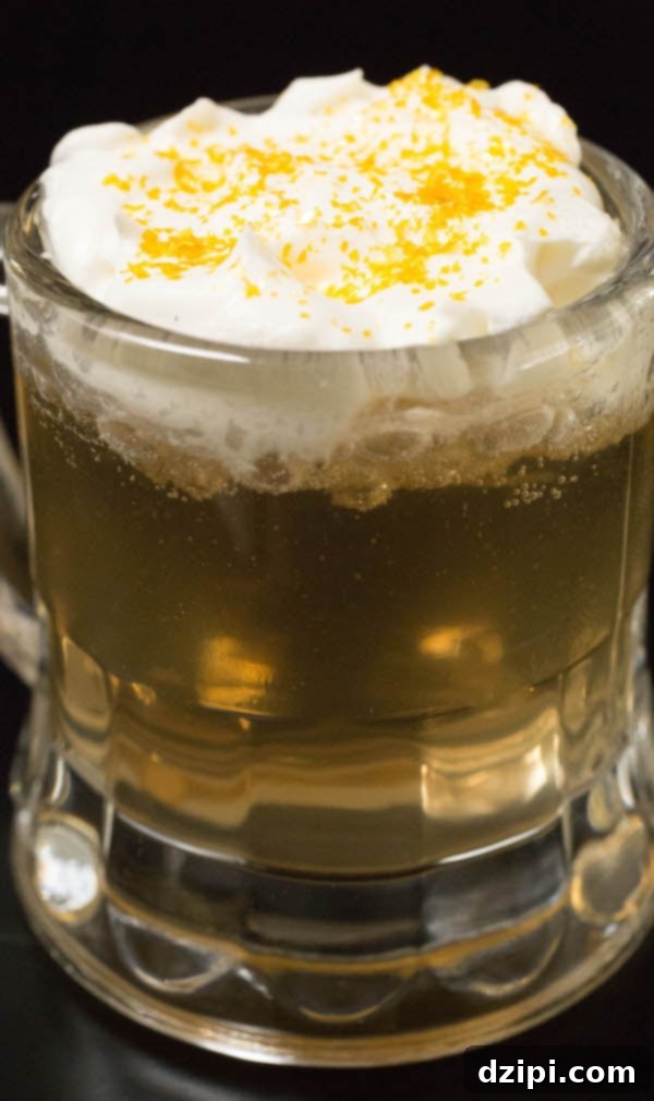 Close up of a butterbeer shot topped with whipped cream and gold glitter, showcasing the magical details.