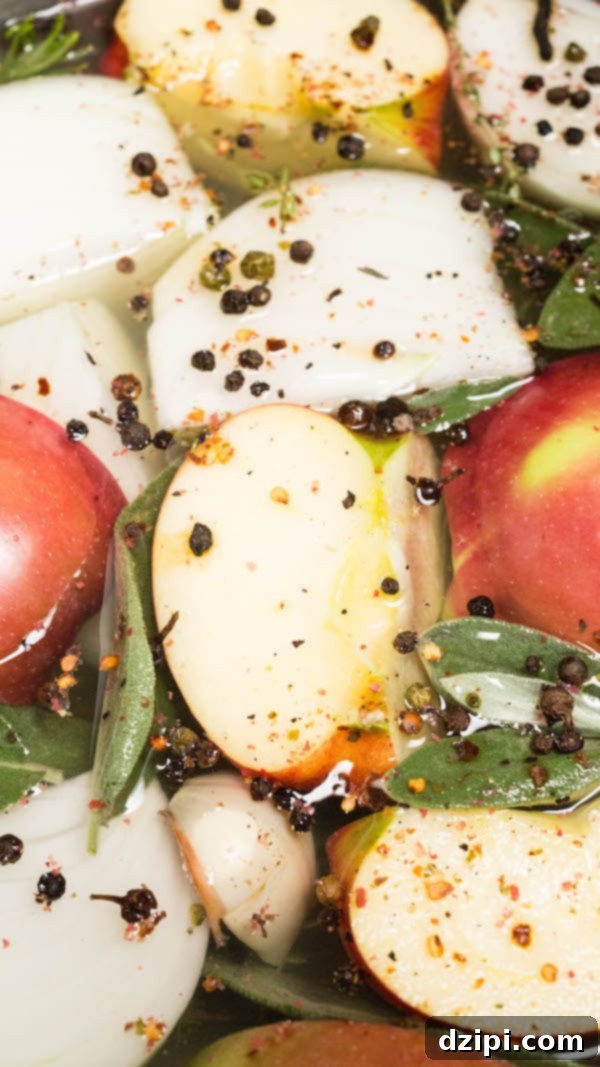 Close-up of red wine turkey brine showing sliced apples, whole peppercorns, and fresh sage leaves floating in the liquid.