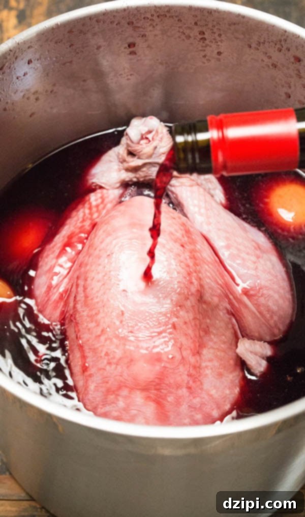Pouring a bottle of red wine over a whole turkey submerged in brine within a large stock pot, preparing for brining.