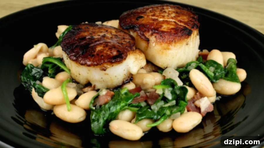 A black dinner plate with two large seared scallops with white beans & spinach, with a slice of lemon on the side.