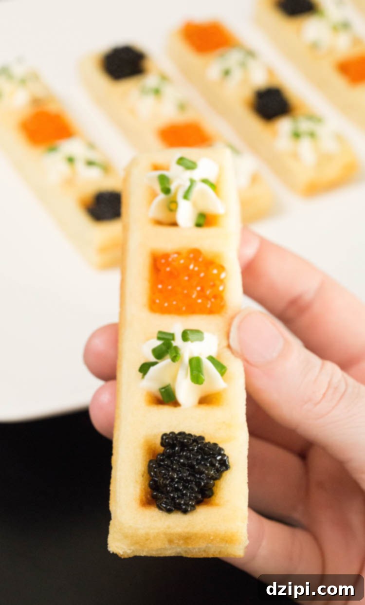 A hand gracefully holds a Caviar Waffle Stick, showcasing its elegant presentation, with a platter of more appetizers in the background.
