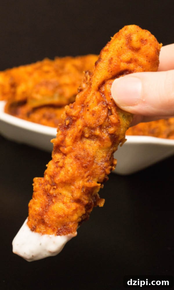 A Nashville Hot Fried Pickle spear, visibly dipped in creamy ranch dressing, highlighting the contrast of flavors.