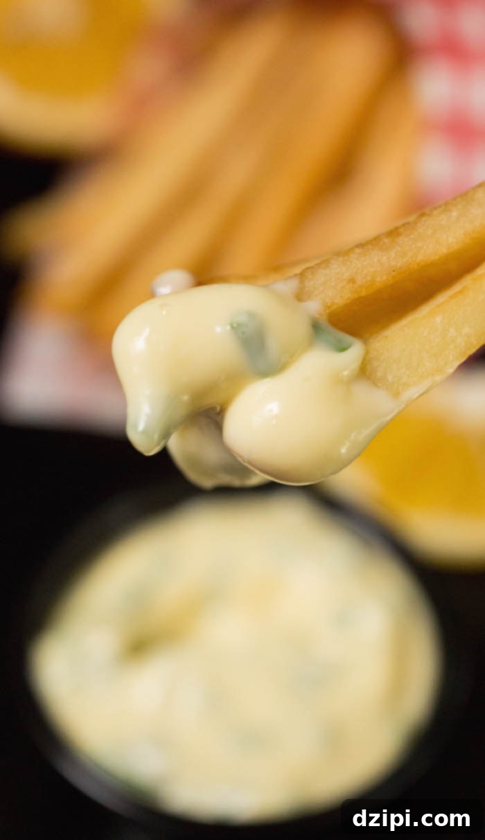 A close-up shot of crispy french fries being dipped into creamy Lemon Chive Mayo, highlighting its perfect texture and appetizing appeal.