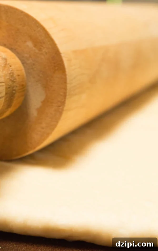 Close up of a wooden rolling pin rolling out pizza dough.