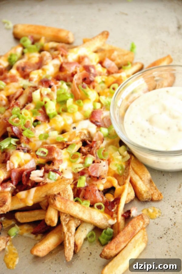Clone Your Favorite Restaurant Meals At Home 22 A pile of fries covered in cheese, bacon, and green onions sits on a sheet pan next to a small bowl of ranch dipping sauce