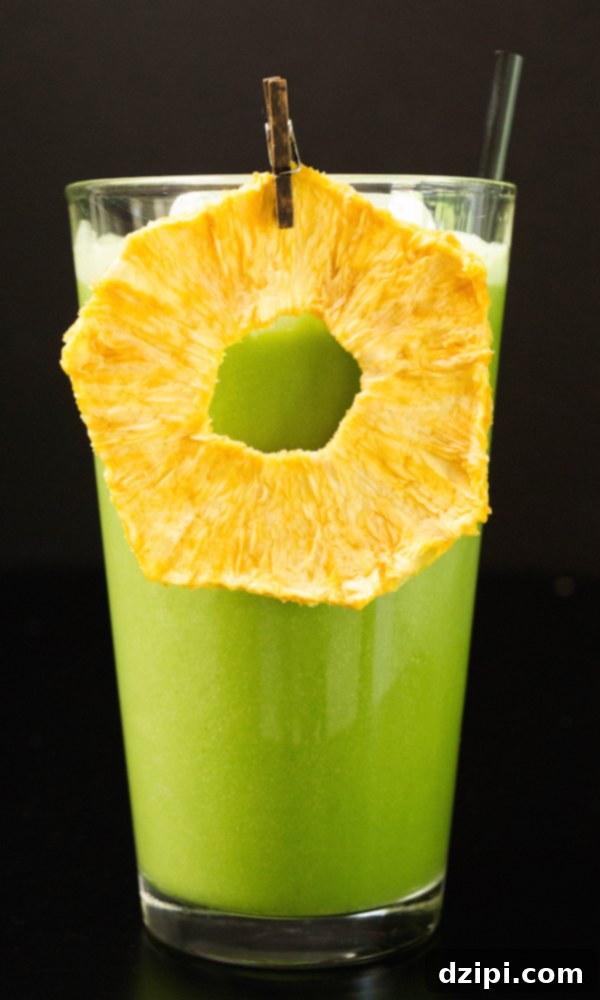 A vibrant green copycat Starbucks Matcha Pineapple Drink in a tall glass, garnished with a dehydrated pineapple slice and served with ice.