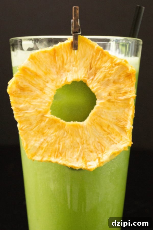 A bright green iced matcha drink, a copycat Starbucks Pineapple Matcha, garnished with a dried pineapple ring, in a tall glass against a dark background.