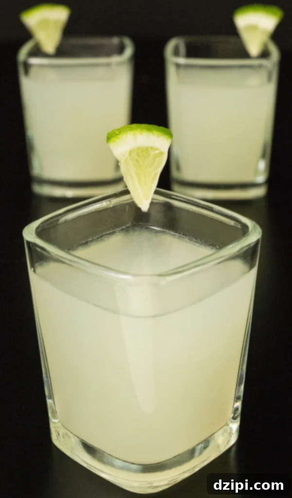 Zesty Lime Shooters 3 Three lime drop shots in square glasses on a sleek black background, garnished with fresh lime wedges.