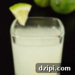 Zesty Lime Shooters 5 A single lime drop shot in a square glass on a black background with two limes.