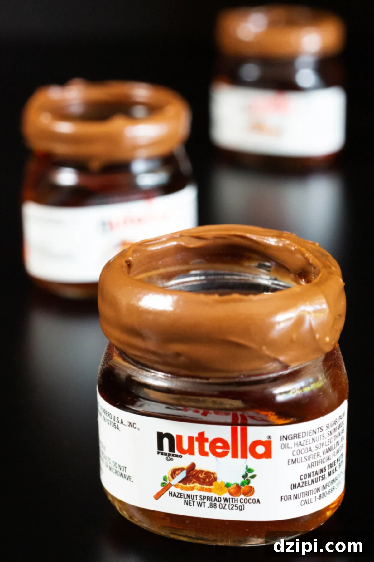 Three miniature Nutella jars filled with shots and rimmed with Nutella spread on a black background.