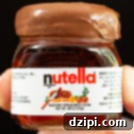 A thumb and index finger hold up a mini Nutella jar that's filled with a Nutella shot. The rim has been dipped in the hazelnut spread.