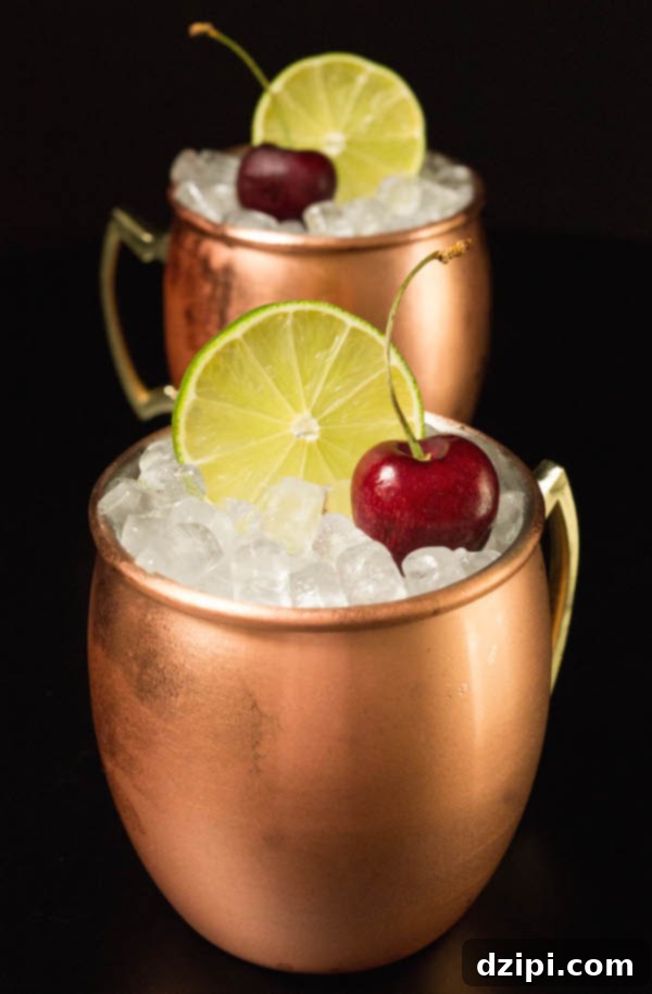 Two cherry limeade moscow mules in copper mugs on a black background