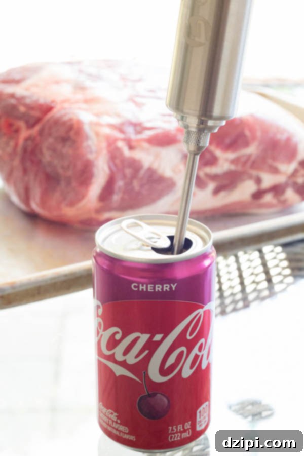 Cherry Cola Smoked Pulled Pork 5 A can of Cherry Coke in the foreground with a meat injector in it. Blurred raw pork shoulder in the background, ready for injection.