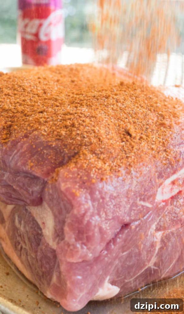 Cherry Cola Smoked Pulled Pork 7 Orange colored BBQ spice rub being generously sprinkled on top of a raw pork shoulder.