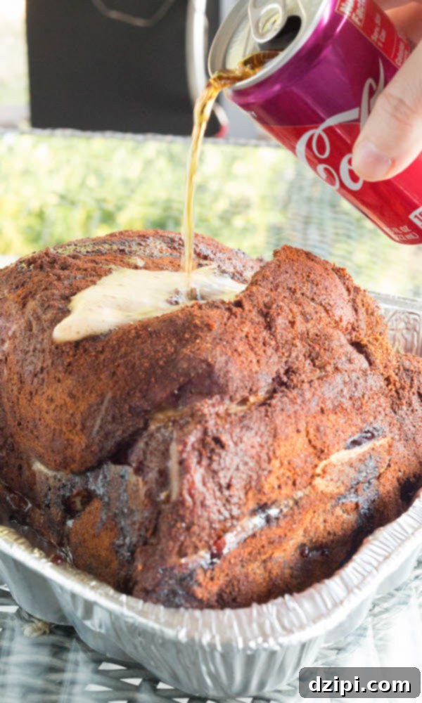 Cherry Cola Smoked Pulled Pork 9 Cherry Coke from a can being poured over the top of a cooked pork shoulder that is sitting in a disposable aluminum pan, ready for wrapping.