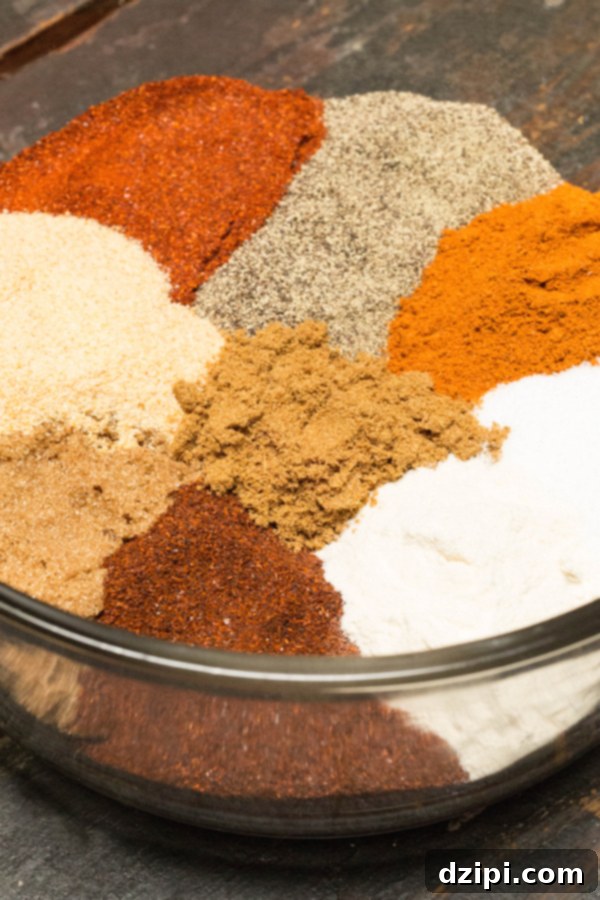 Multi-colored spices for BBQ spice rub, including paprika, chili powder, and brown sugar, artfully arranged in separate piles within a large glass bowl.