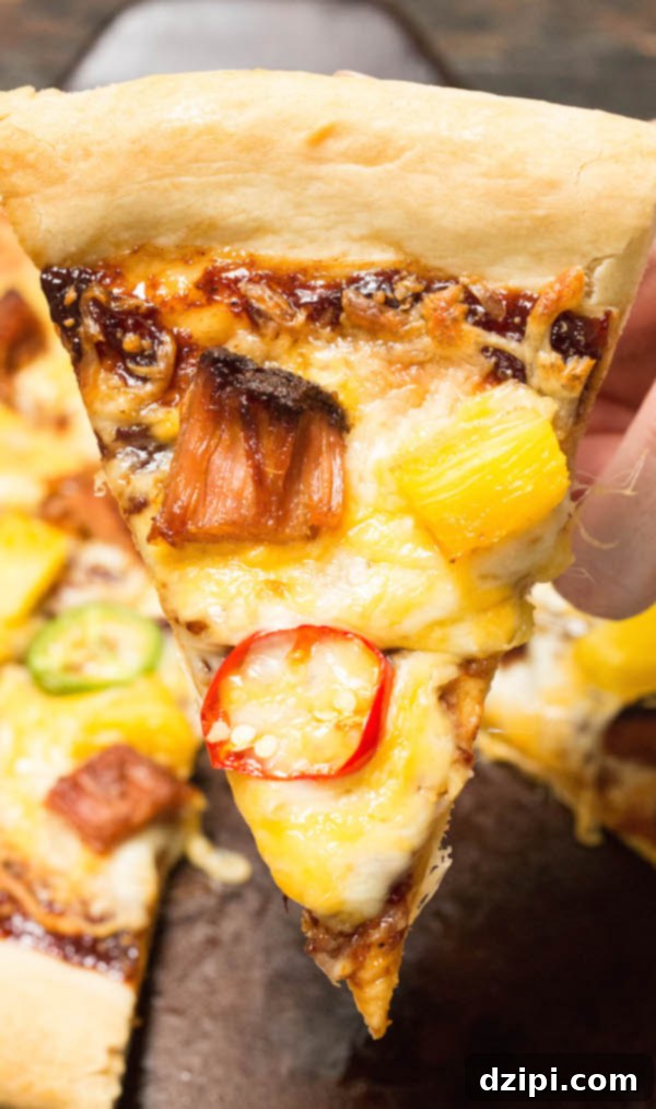 Tropical BBQ Pulled Pork Pizza 4 A close-up shot of a hand holding a single slice of homemade Pulled Pork & Pineapple BBQ Pizza, showcasing the golden-brown crust, melted cheese, visible chunks of smoked pineapple, slices of jalapeño, and tender pulled pork, dripping with deliciousness.