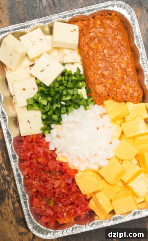 Overhead shot of a disposable pan filled with cheese, chorizo, onions, jalapeños, and canned tomatoes, perfectly arranged to make smoked queso.