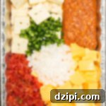 Overhead shot of a pan filled with sliced Velveeta, pepper jack, jalapeños, onion, Rotel, and chorizo, showcasing the ingredients for delicious smoked queso.