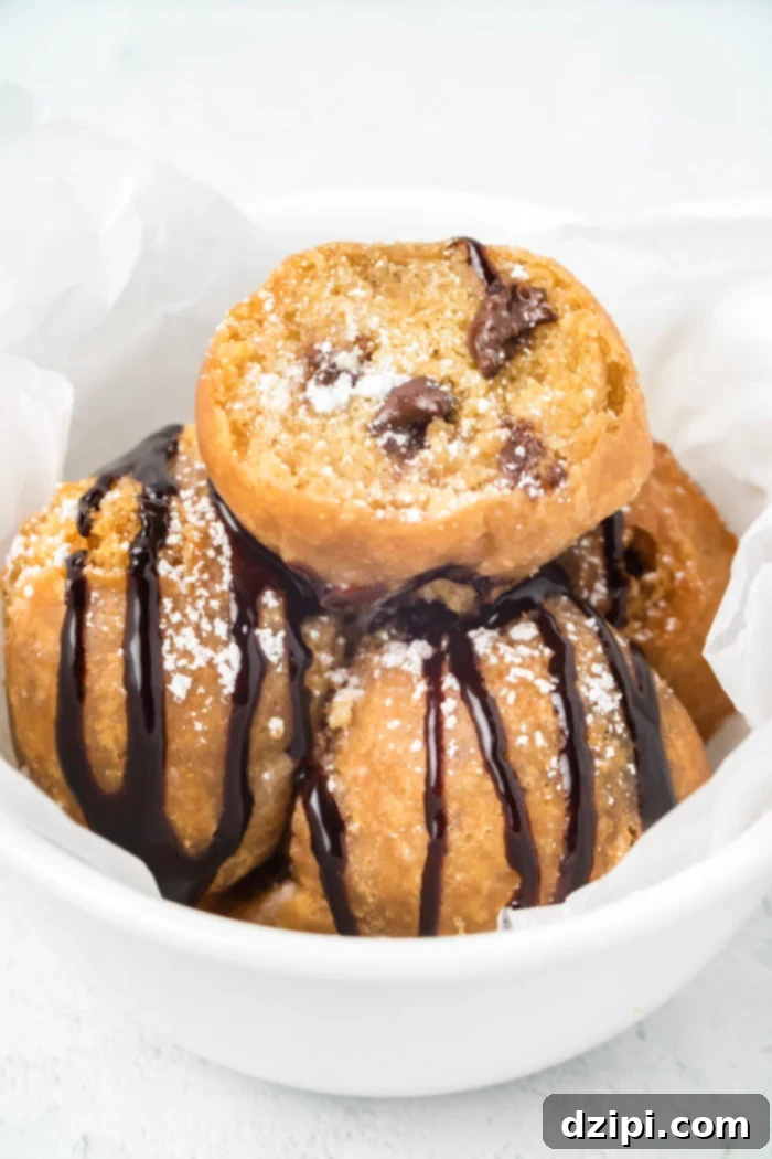 A bowl of golden deep-fried cookie dough balls covered in rich chocolate syrup and powdered sugar, ready to be enjoyed.