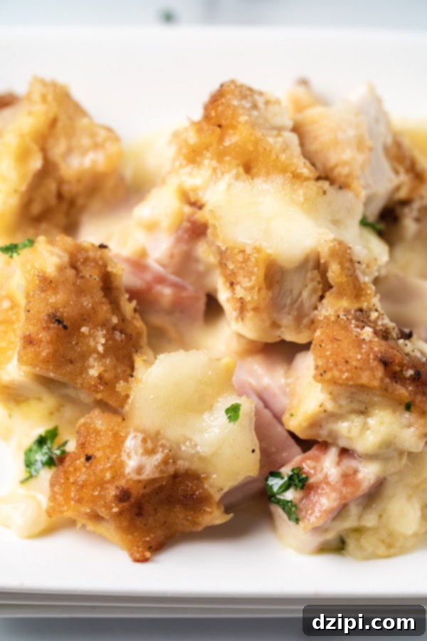 Close up of a piece of Chicken Cordon Bleu Casserole on a white dish, showing layers of chicken, ham, and melted Swiss cheese