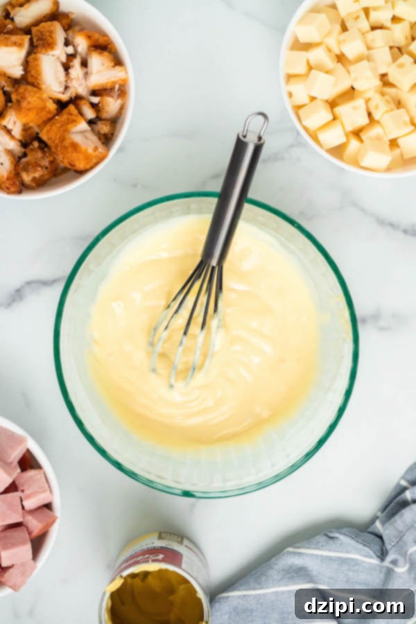 Overhead shot of separate bowls containing popcorn chicken, cubed Swiss cheese, diced ham, and cream of chicken soup, arranged on a marble board