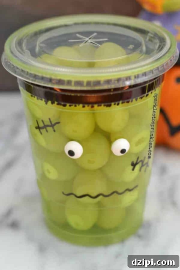 A clear plastic cup decorated with a Sharpie to resemble Frankenstein's monster, filled with refreshing green grapes