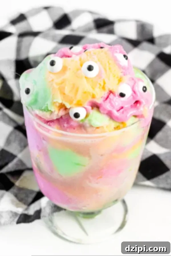 Multi-colored sherbet ice cream served in a clear glass cup, adorned with playful monster eyeballs on top