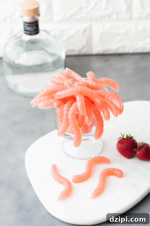 A clear glass bowl brimming with bright pink, homemade strawberry margarita gummy worms, perfect for an adult Halloween treat