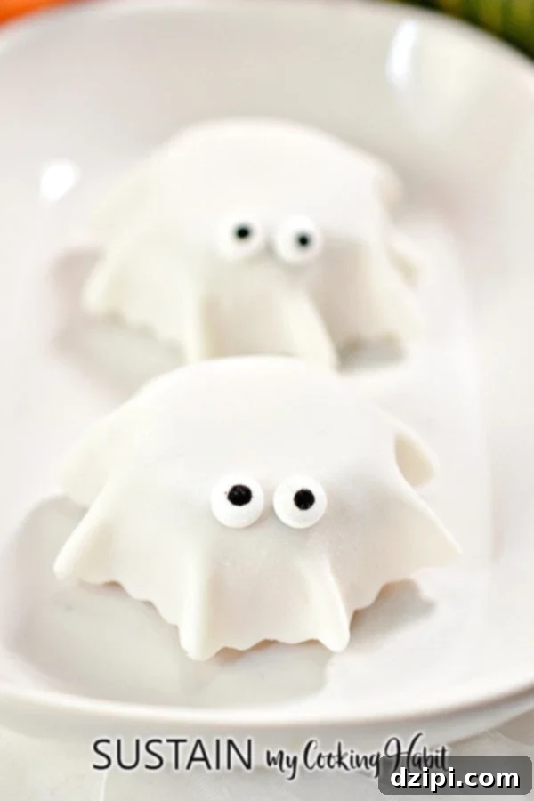 Mini muffins draped with white fondant and adorned with candy eyes, cleverly designed to resemble adorable little ghosts