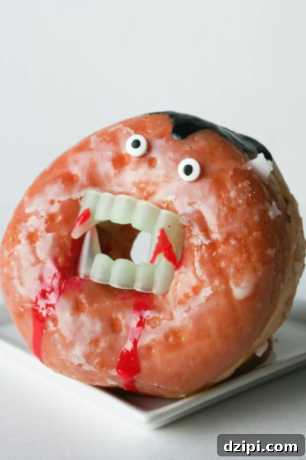 A glazed donut standing vertically, transformed into a vampire with plastic fangs in the hole and candy eyes on top