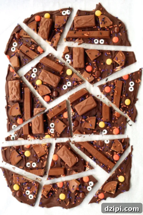 Overhead shot of rich chocolate bark, generously adorned with bite-sized candy bars, whimsical candy eyes, and festive black & orange sprinkles