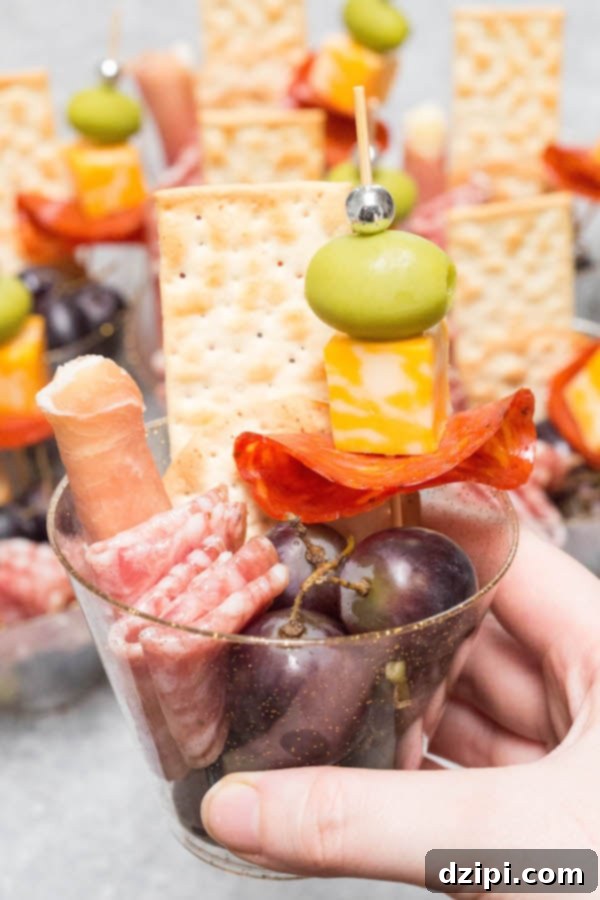 A close-up of a hand holding a perfectly packed charcuterie cup, featuring folded prosciutto, cheddar cubes, olives, and fresh grapes, ready to enjoy at a holiday party.