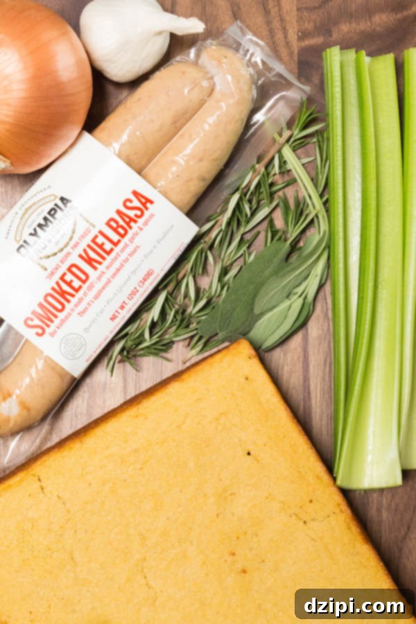 The ingredients for cornbread & sausage stuffing lie on a wood cutting board. A package of smoked kielbasa, rosemary, sage, celery, yellow onion, garlic, cornbread