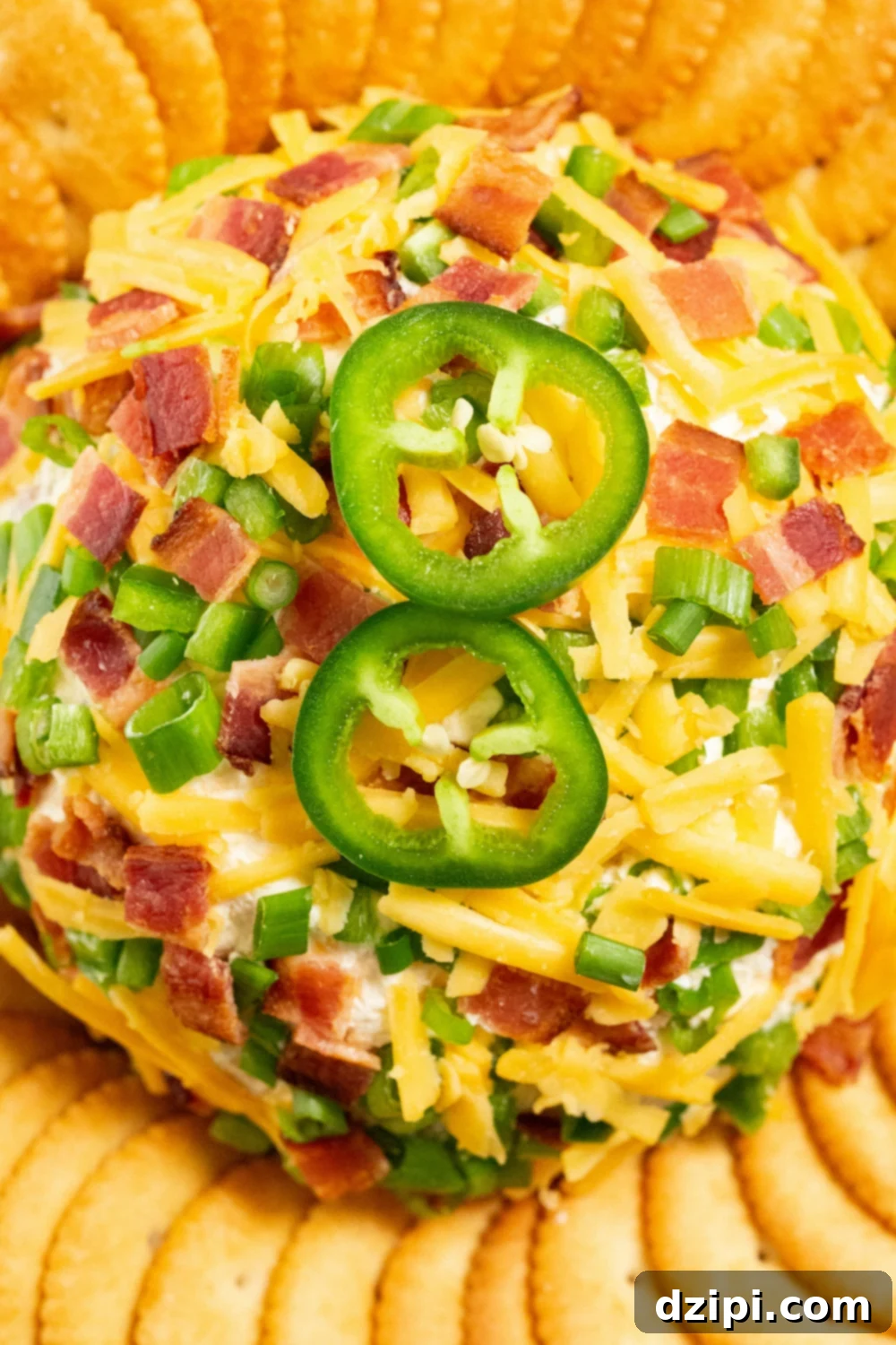 Overhead shot of a jalapeno popper cheeseball covered in shredded cheddar, diced jalapeños, and chopped bacon