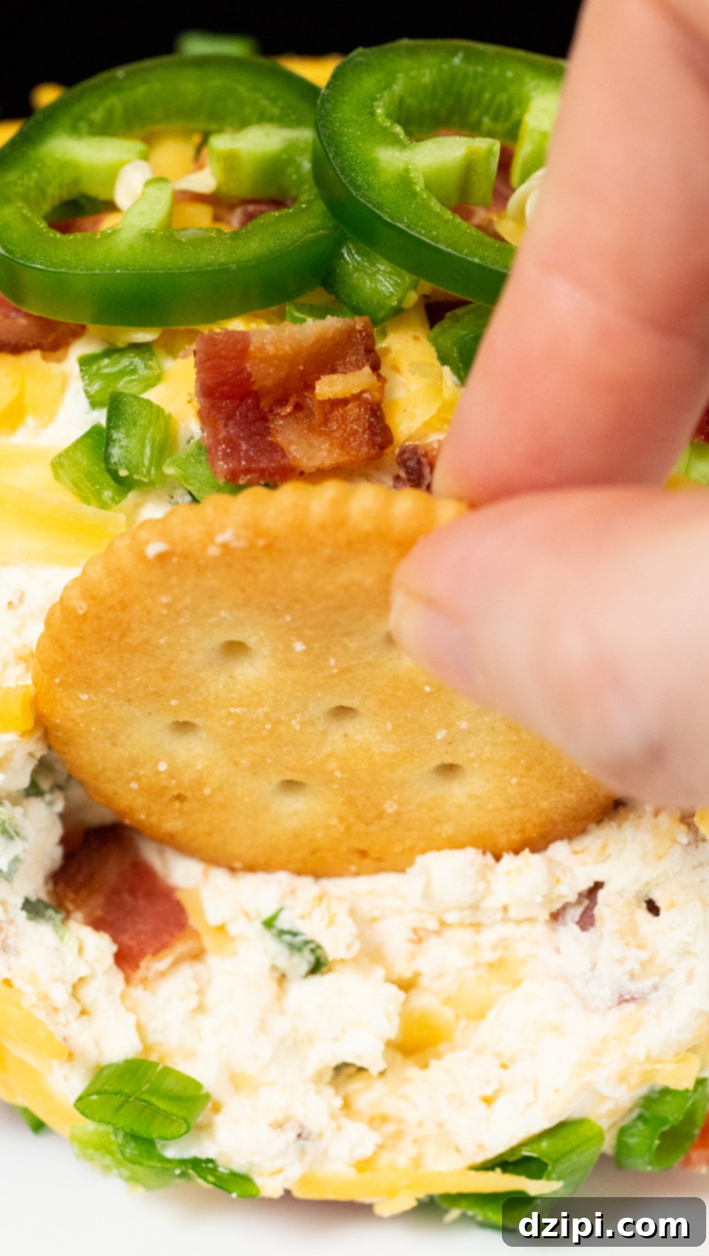 Close up of a ritz cracker being dipped in a jalapeno popper cheese ball