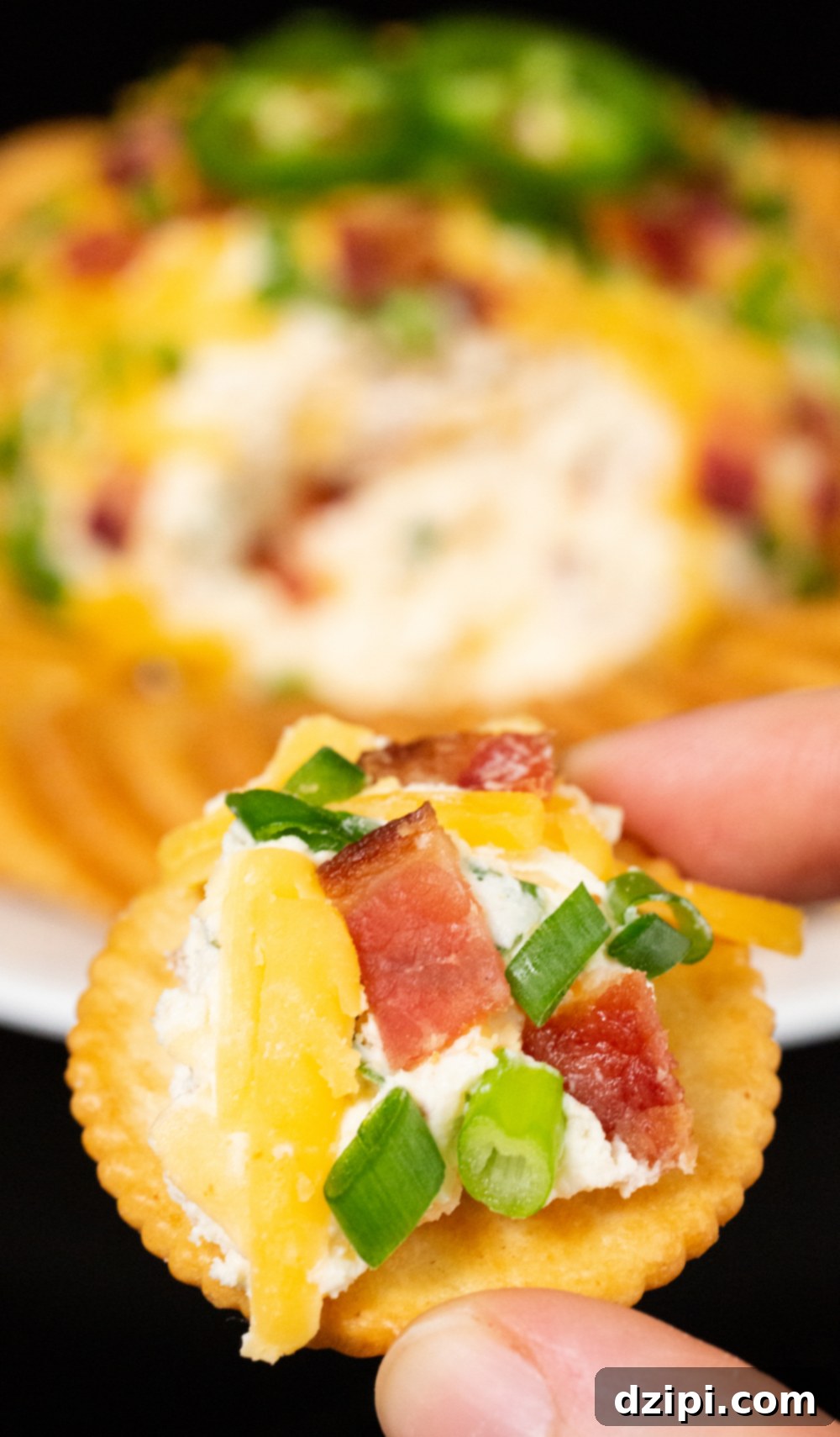 Two fingers hold up a ritz cracker with jalapeño popper cheese ball spread over the top. 