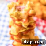 A Korean French Fry Corn Dog, coated in crispy fries, drizzled with yellow mustard and red ketchup, with a bite taken out to reveal the juicy hot dog inside.