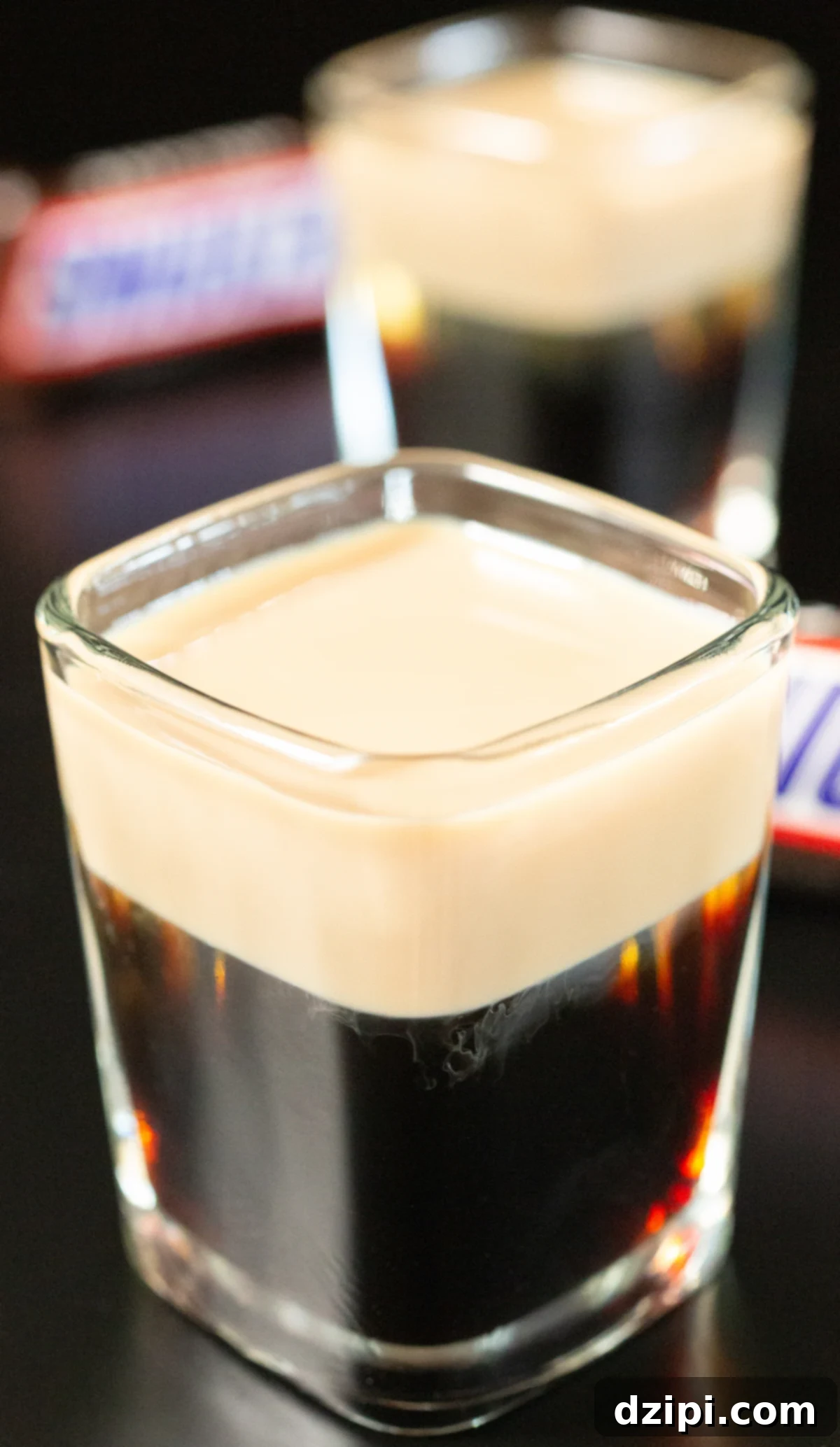 Snickers Shooter 5 Two perfectly layered Snickers shots are displayed on a dark background, with a blurred Snickers candy bar in the background, making a clear connection to the inspiration.