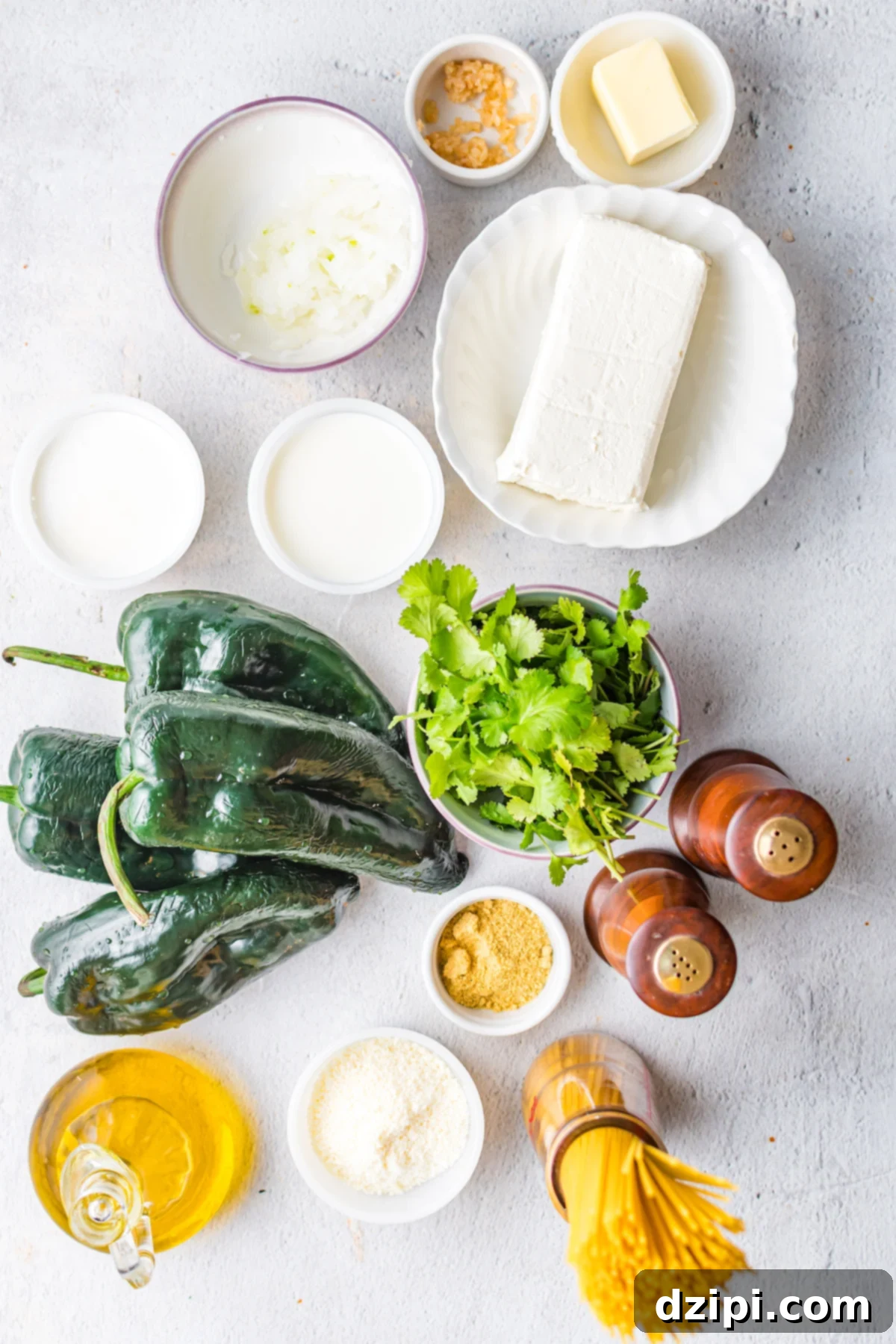 An overhead shot showcasing all the fresh, colorful ingredients required to make delicious green Mexican spaghetti, including vibrant poblanos, creamy cheese, fragrant cilantro, dry spaghetti, and seasoning.