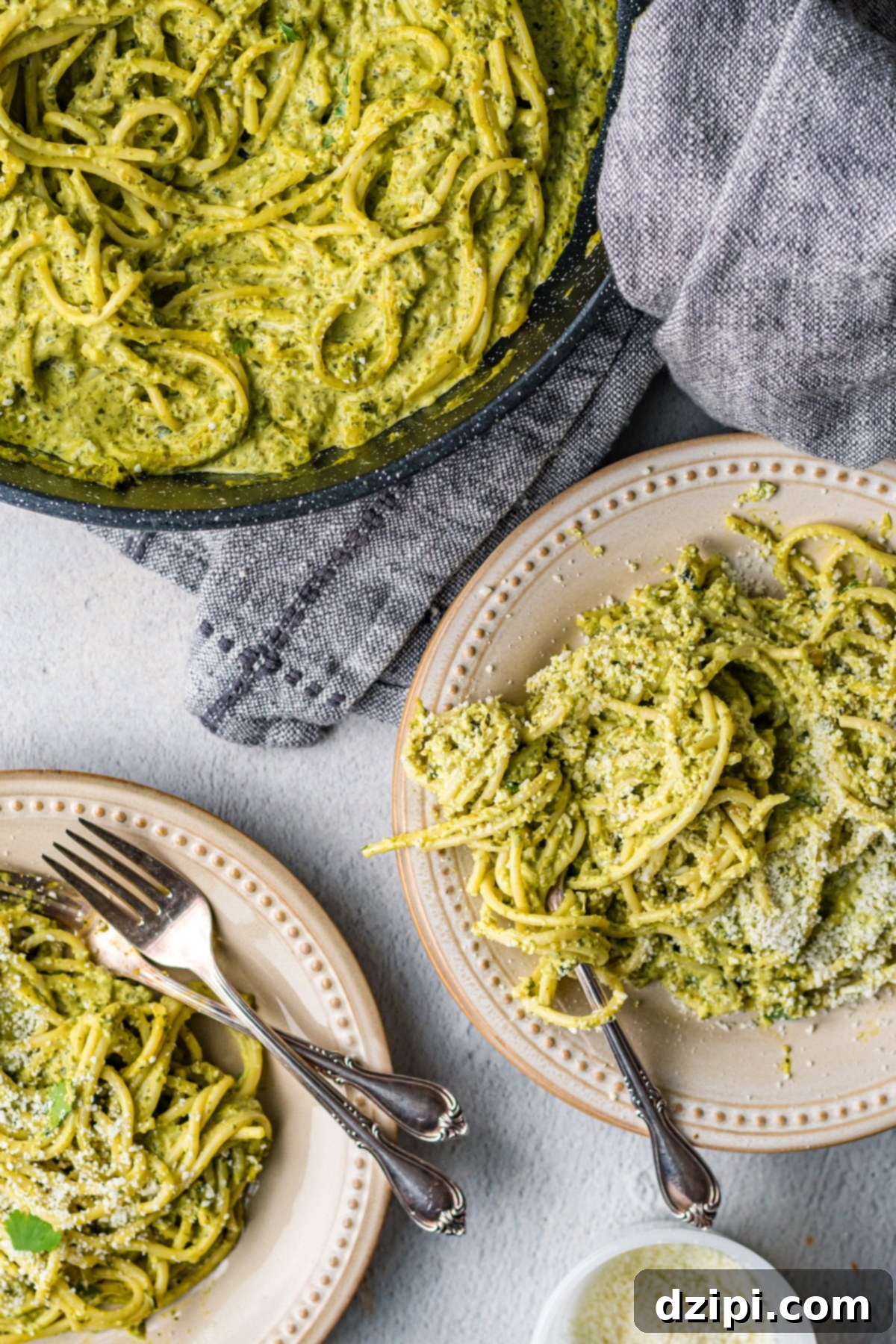 An inviting overhead view of two plates of vibrant green Mexican spaghetti, artfully arranged beside a large pan filled with the creamy pasta.