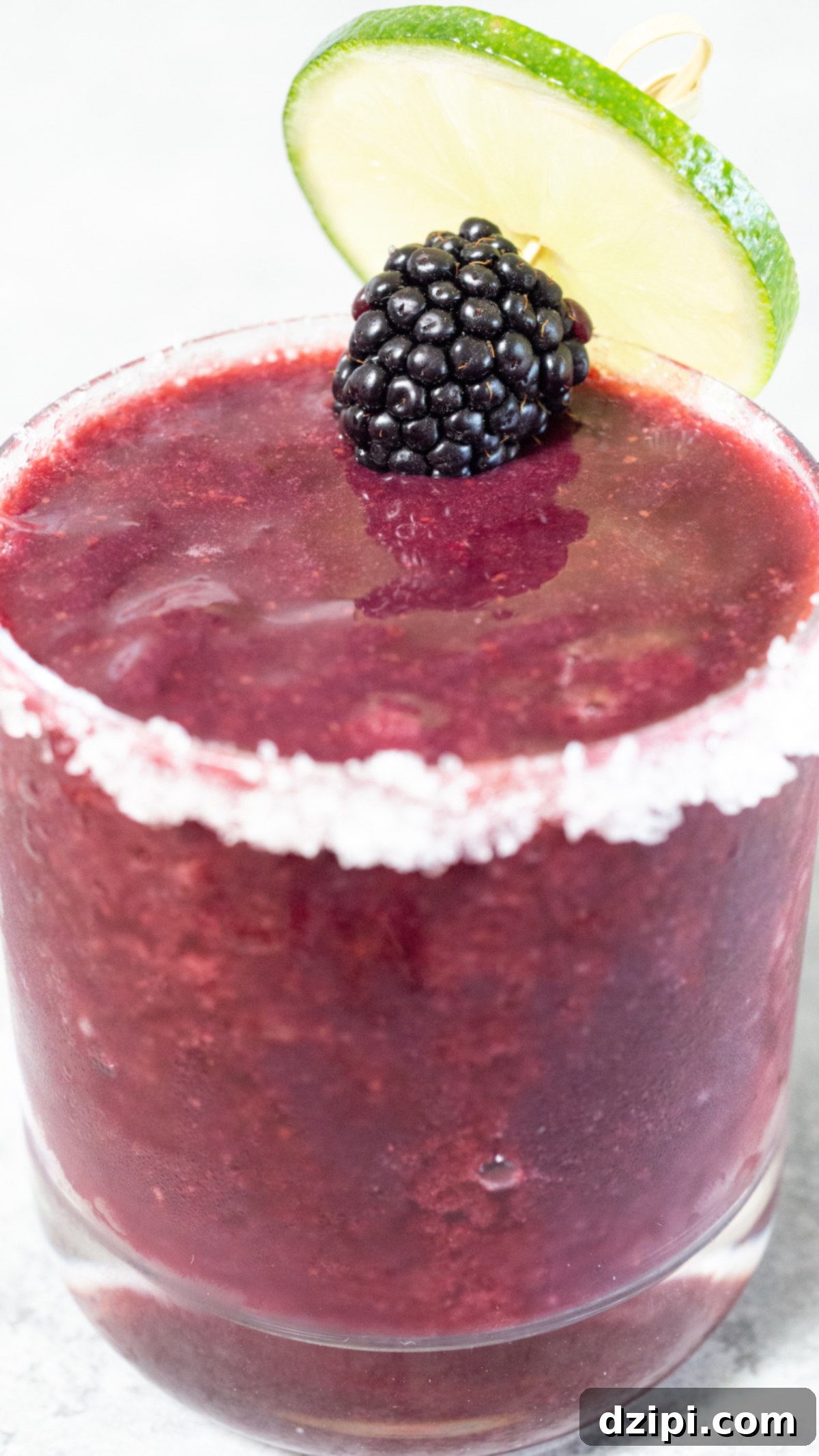 A close-up of a stunning purple blackberry margarita presented in a sophisticated short glass, elegantly garnished with a single fresh blackberry and a delicate lime wheel. The drink looks perfectly chilled and inviting.