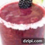 A purple blackberry margarita in a short glass garnished with a blackberry and lime wheel.