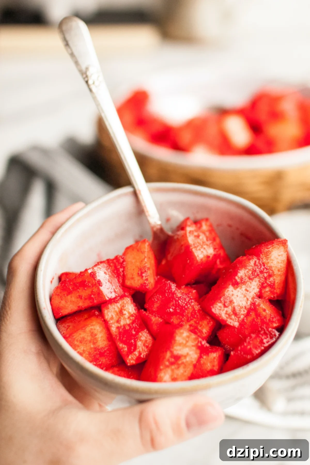 A hand holds a light colored bowl filled with chopped apples that have been covered in red jello.