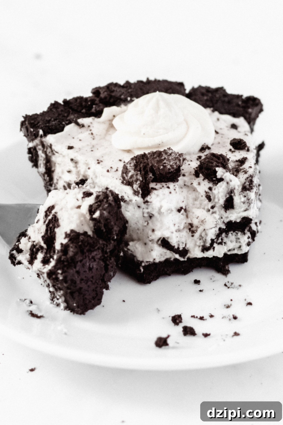 Decadent Oreo Cream Pie 5 A delectable slice of cookies & cream pie with a forkful taken out of it sits on a clean white plate on a white background, inviting a taste.
