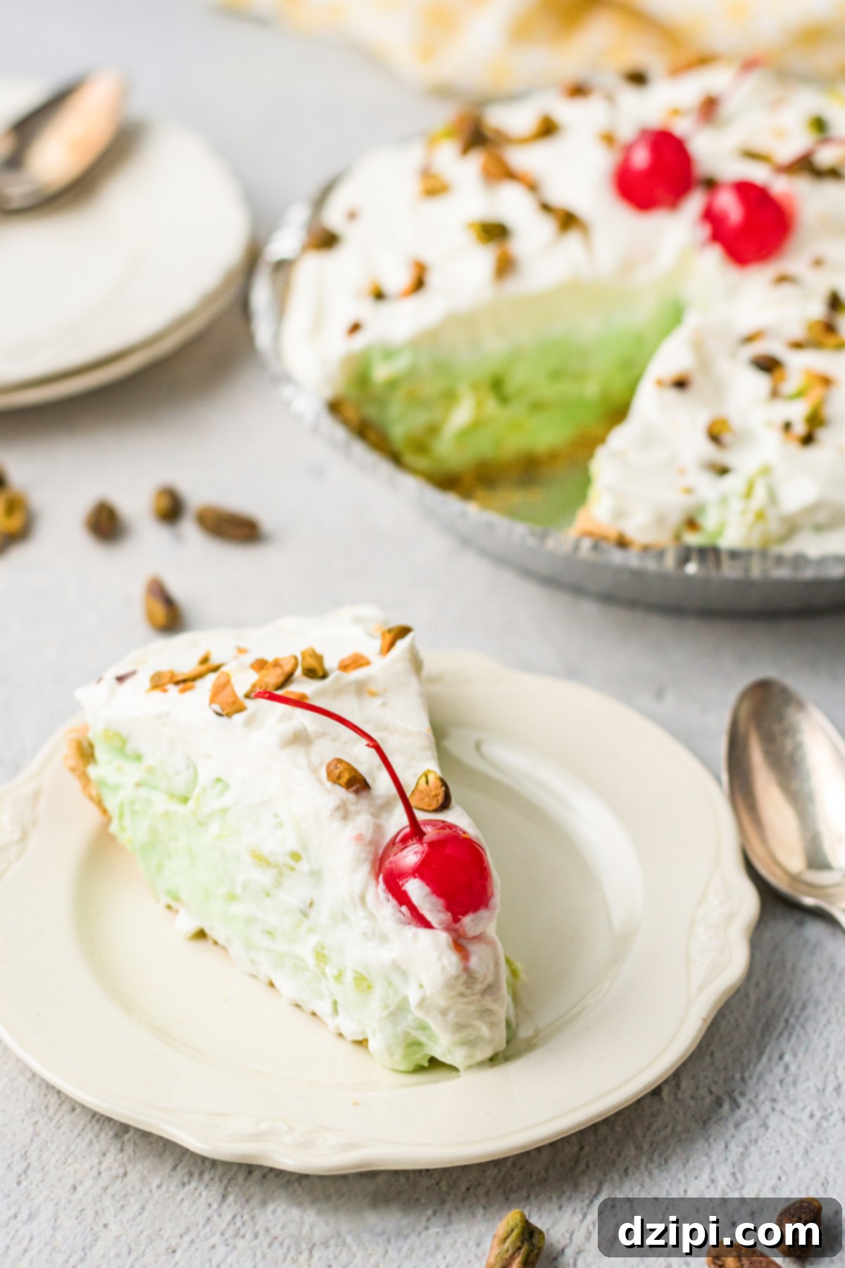 Emerald Dream Pie 3 A perfectly sliced piece of pistachio pie, adorned with a single maraschino cherry, rests on a small dessert plate beside the remaining pie.