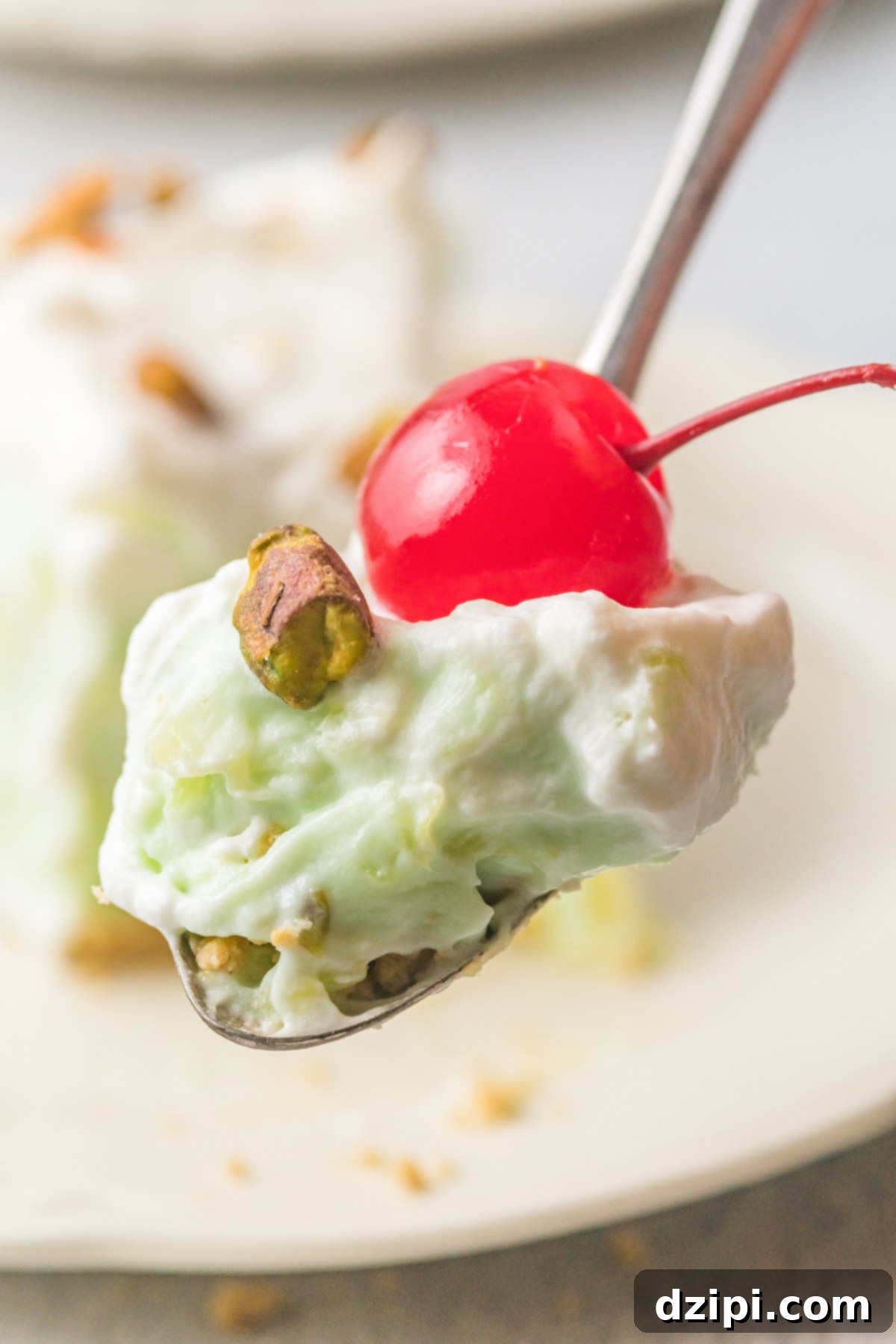 Emerald Dream Pie 6 A spoon delicately holds a perfect bite of pistachio pie, topped with a bright maraschino cherry. The rest of the pie is beautifully blurred in the background.
