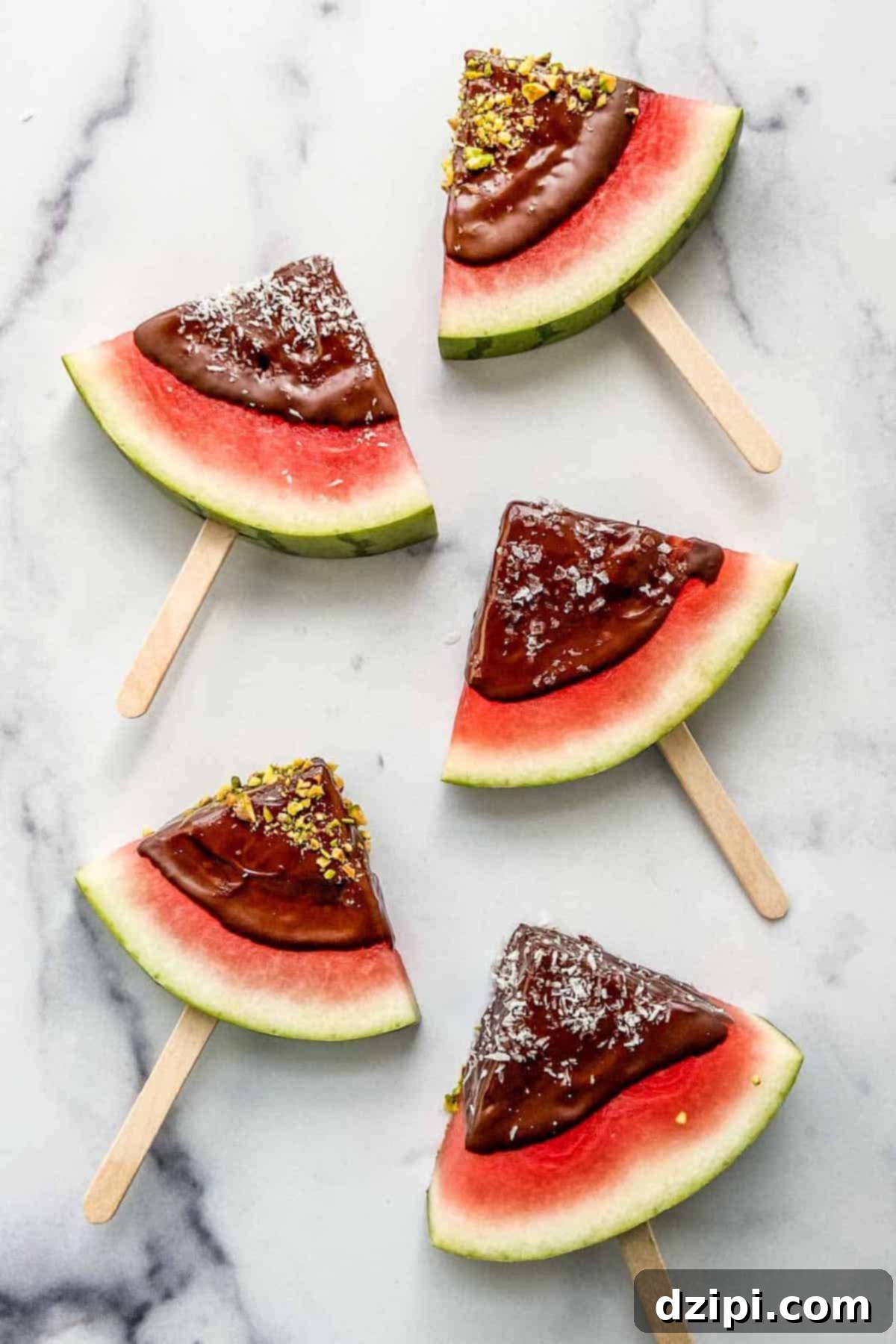 Overhead view of juicy watermelon slices, each dipped in dark chocolate and served on convenient popsicle sticks.